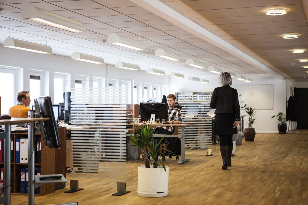 A woman walks through an office, passing a desk adorned with a plant, showcasing a professional environment